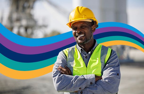 a construction worker wearing a hard hat and safety vest is smiling with his arms crossed .