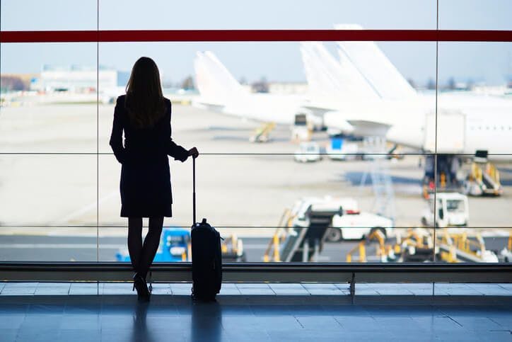 woman with luggage at airports looking out the window at planes
