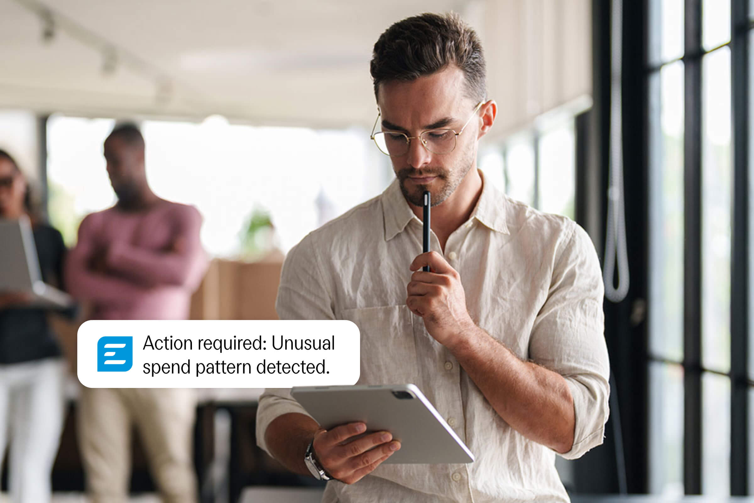 A man looks at a tablet displaying a notification: "Action required: Unusual spend pattern detected."