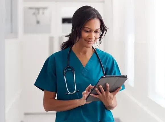 a nurse is using a tablet computer in a hospital hallway .