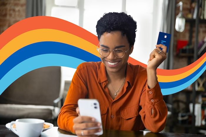 a woman is sitting at a table holding a credit card and a cell phone .