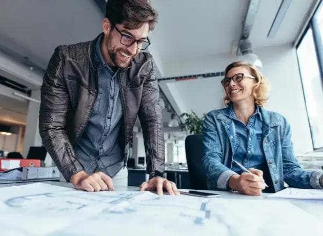 a man and a woman are looking at a blueprint together in an office .