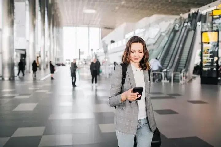 a woman is walking through an airport looking at her cell phone .