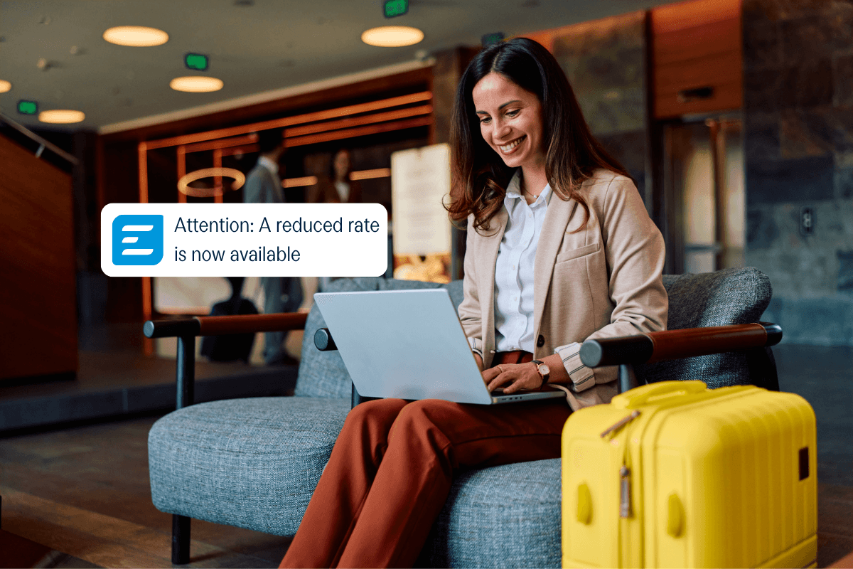 A smiling woman on a laptop in a lounge receives a notification bubble stating 'Attention: A reduced rate is now available'.